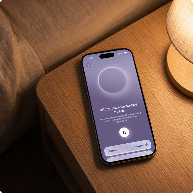 Smartphone displaying a white noise app on a wooden nightstand.