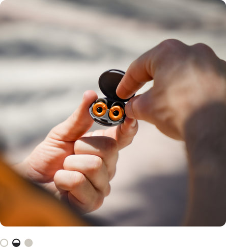 A close-up of a person holding an open McLaren x Loop Switch 2 earplug case, photographed outdoors against a blurred background.