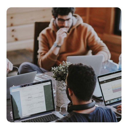 Image of a desk with three people working on it on laptops.