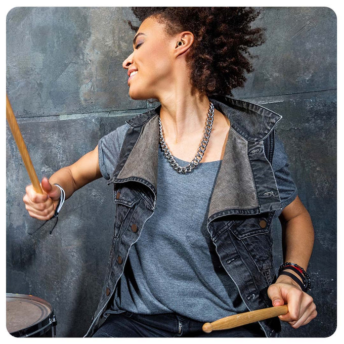 Image of a woman playing the drums enthusiastically, wearing Loop earplugs.