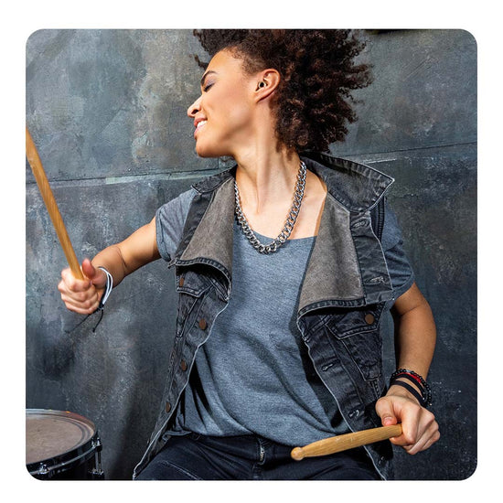 Image of a woman playing the drums enthusiastically, wearing Loop earplugs.