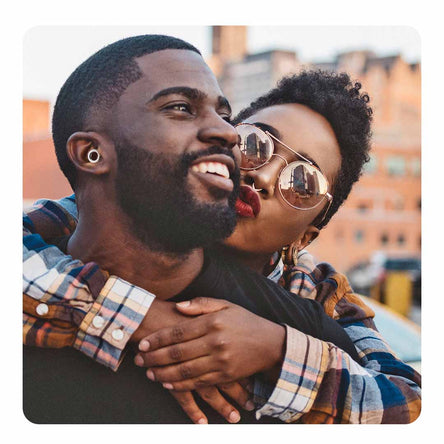 Image of a man and a women smiling together with her holding him over the shoulders. He is wearing Loop ear plugs.