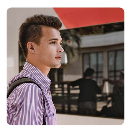 Image of a man wearing his backpack in a space where there are more people, wearing  Loop earplugs.