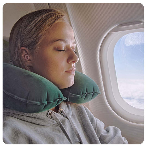 A woman resting her head in a travel pillow on an airplane while wearing Loop earplugs.