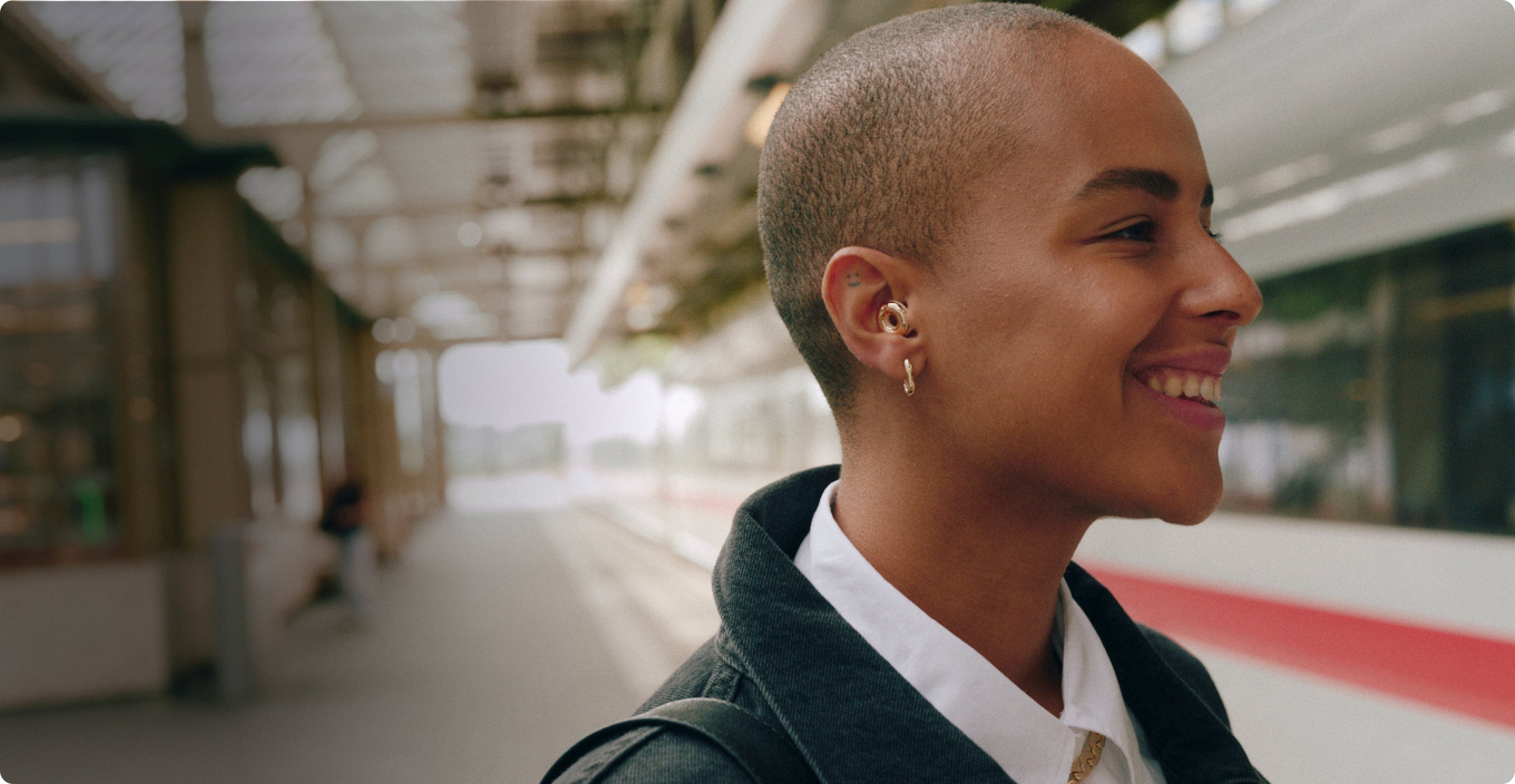 Woman with a shaved head smiling wearing Loop Switch 2 in a train station