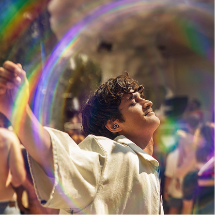 Person in a large bubble containing rainbow colors, surrounded by people in a festival setting.